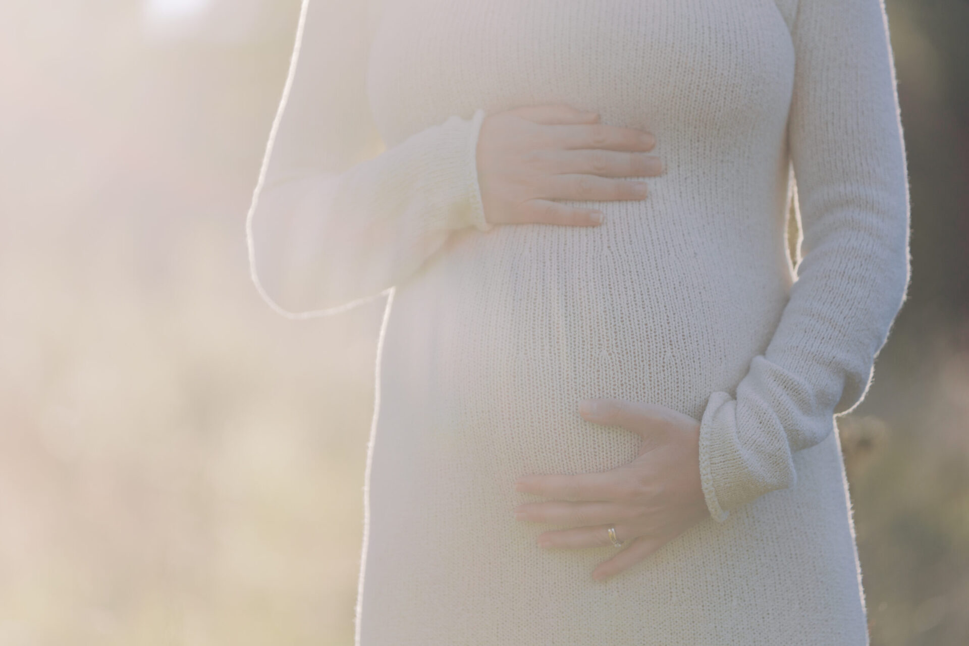gravid mage mor holder rundt magen med solskinn i bakgrunn